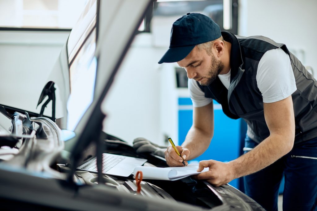 Auto mechanic writing data while examining engine at repair shop.